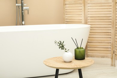 Photo of Reed diffuser and vase on table in bathroom. Space for text