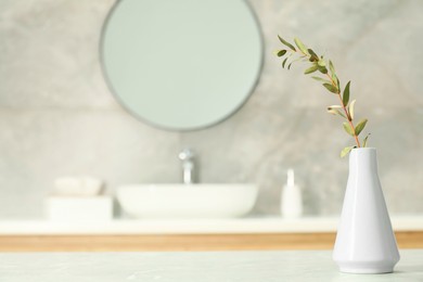 Photo of Vase with green twig on light grey marble table in bathroom, space for text