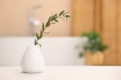 Vase with green twig on light wooden table in bathroom, space for text