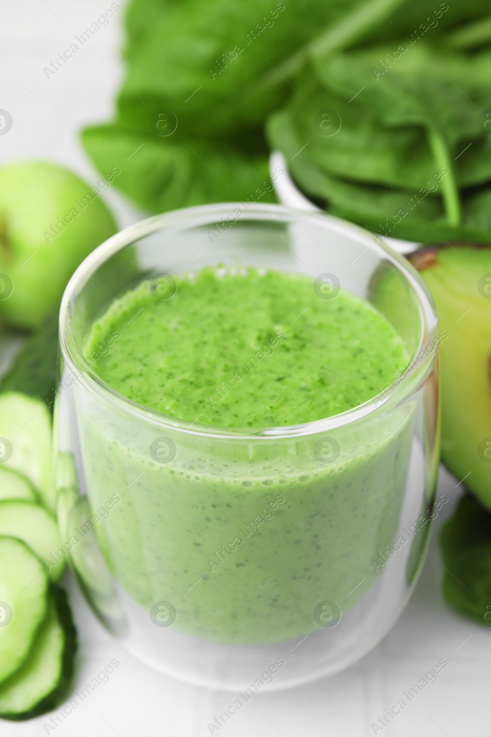 Photo of Tasty green smoothie in glass and products on white tiled table, closeup