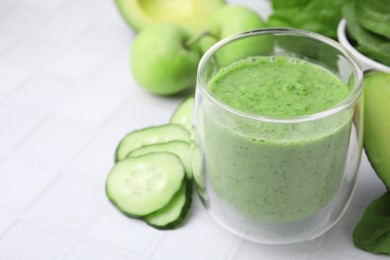 Photo of Tasty green smoothie in glass and products on white tiled table, closeup. Space for text