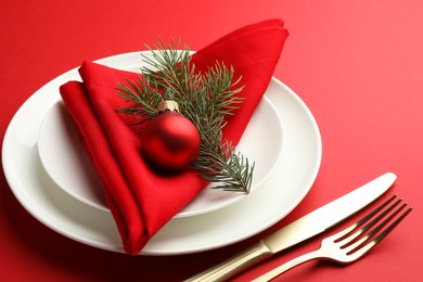 Photo of Beautiful Christmas setting with plates, elegant cutlery and festive decor on red table