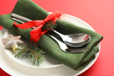 Photo of Beautiful Christmas setting with plates, elegant cutlery and festive decor on red table, closeup