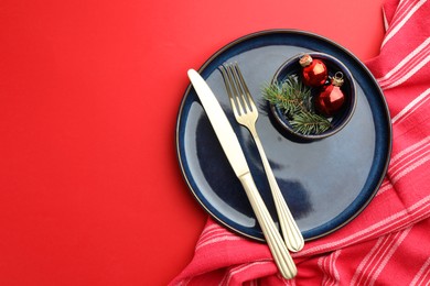 Photo of Beautiful Christmas setting with plate, elegant cutlery and festive decor on red table, flat lay. Space for text