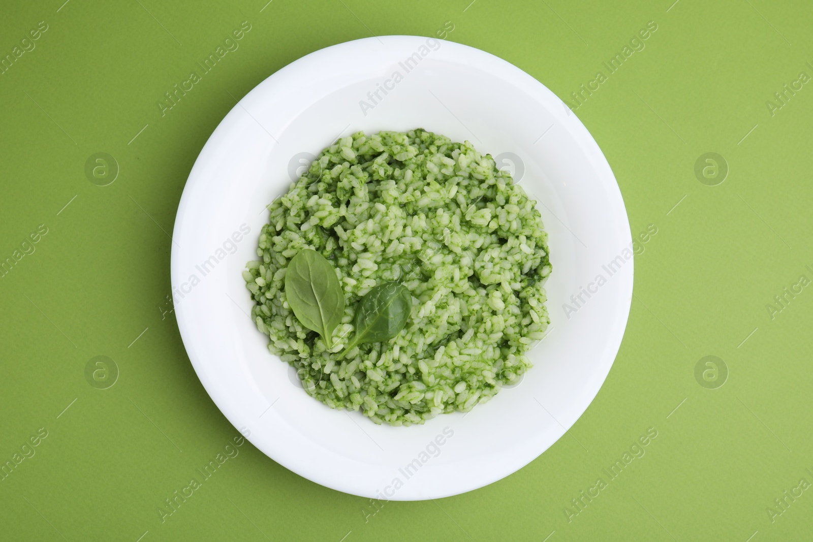 Photo of Delicious spinach risotto on light green background, top view