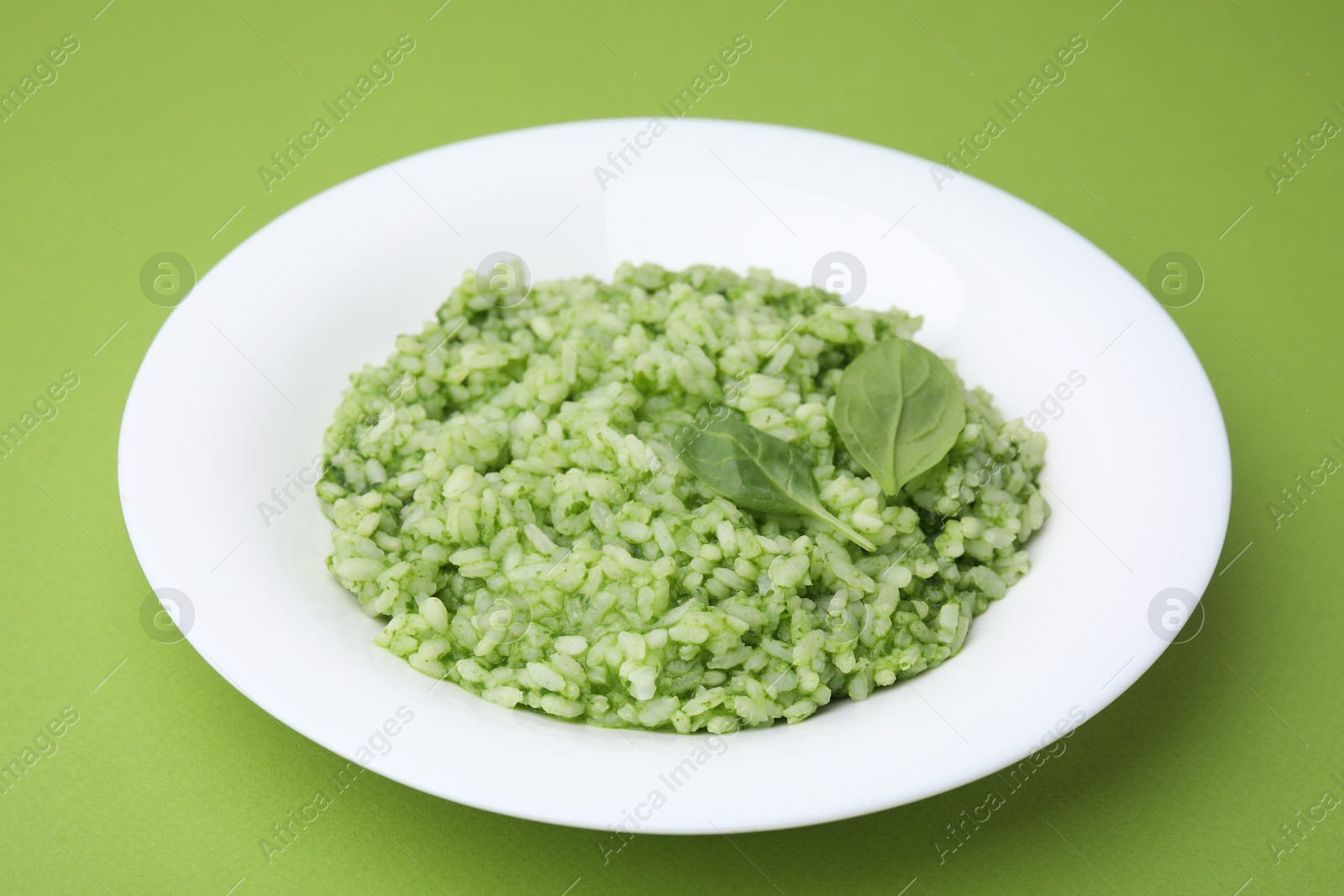 Photo of Delicious spinach risotto on light green background