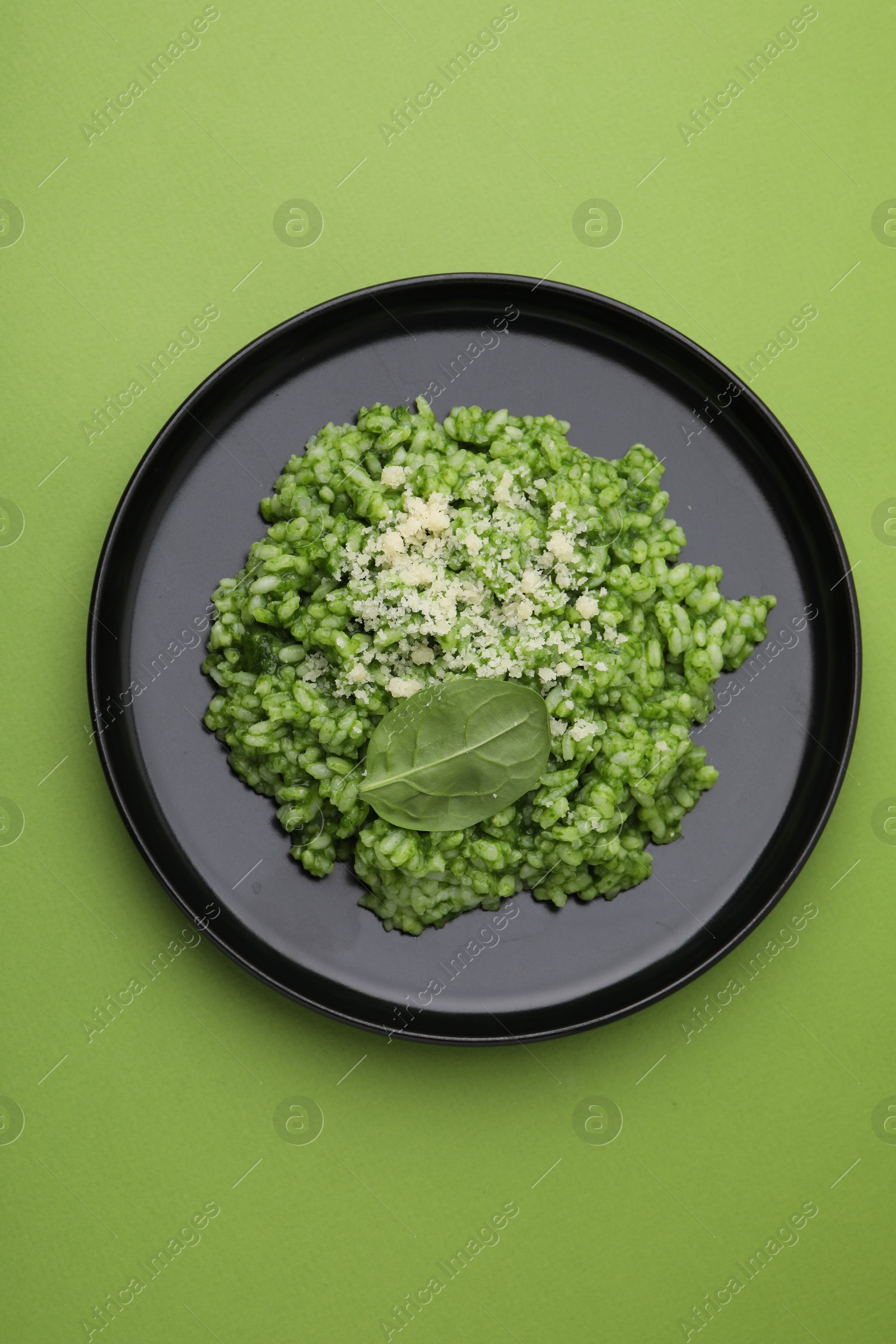 Photo of Delicious spinach risotto with parmesan cheese on light green background, top view