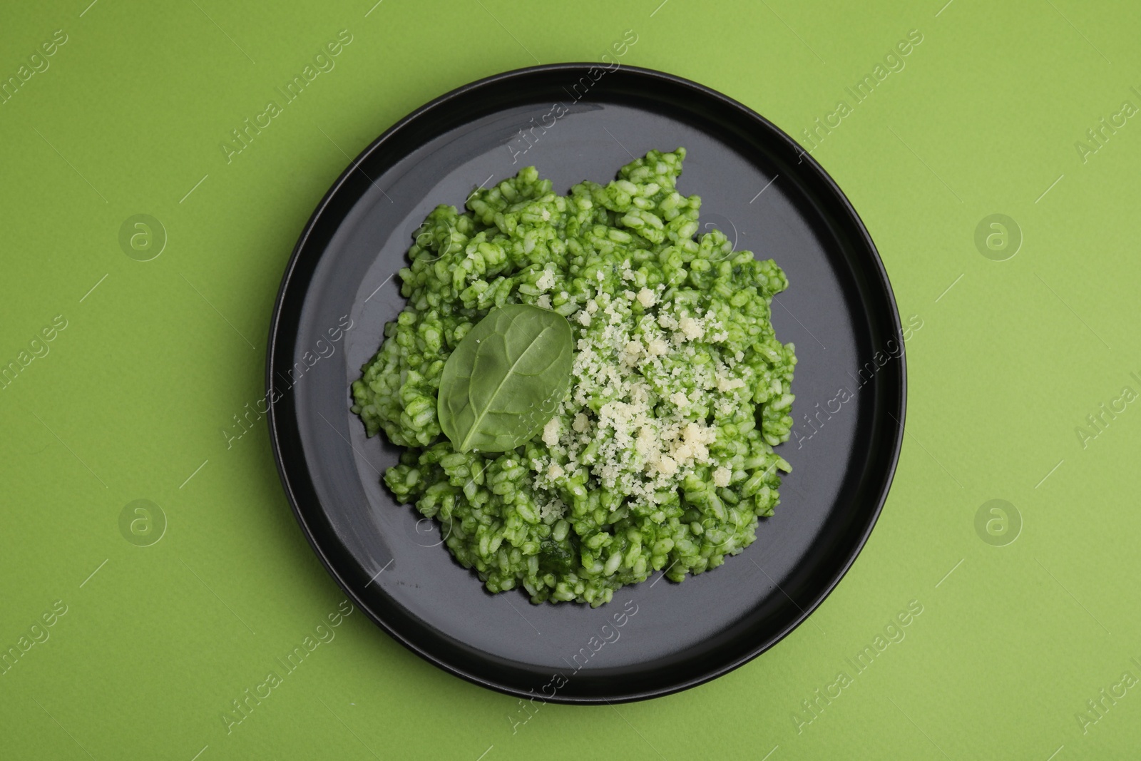 Photo of Delicious spinach risotto with parmesan cheese on light green background, top view