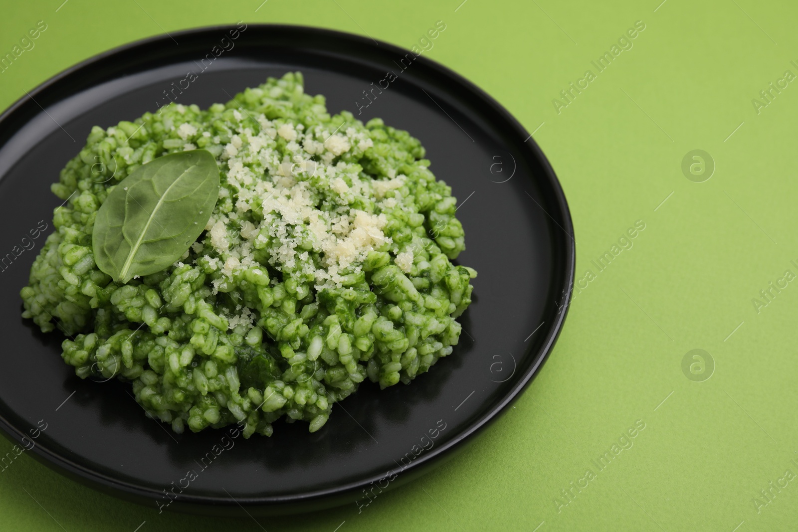 Photo of Delicious spinach risotto with parmesan cheese on light green background, closeup