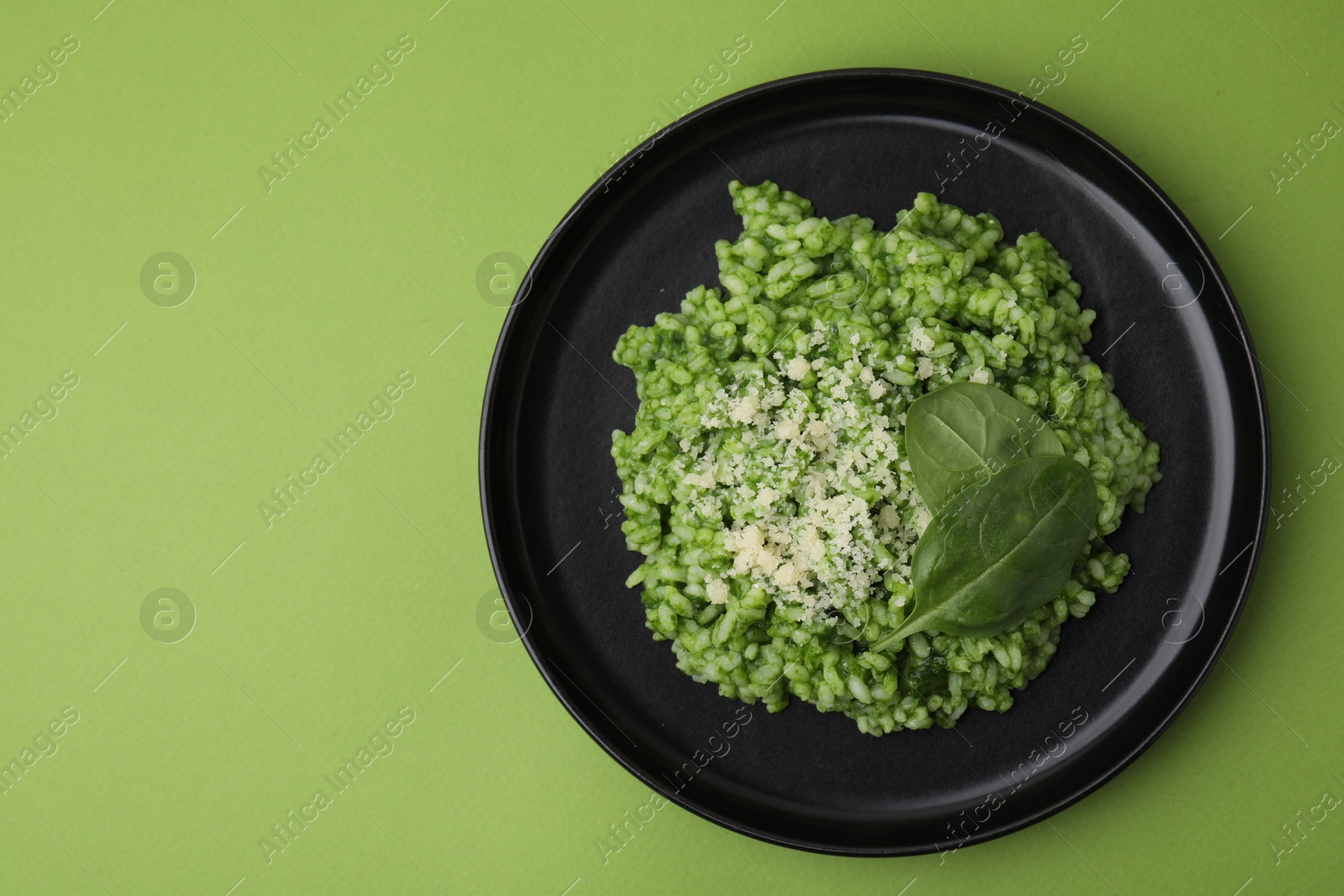 Photo of Delicious spinach risotto with parmesan cheese on light green background, top view. Space for text