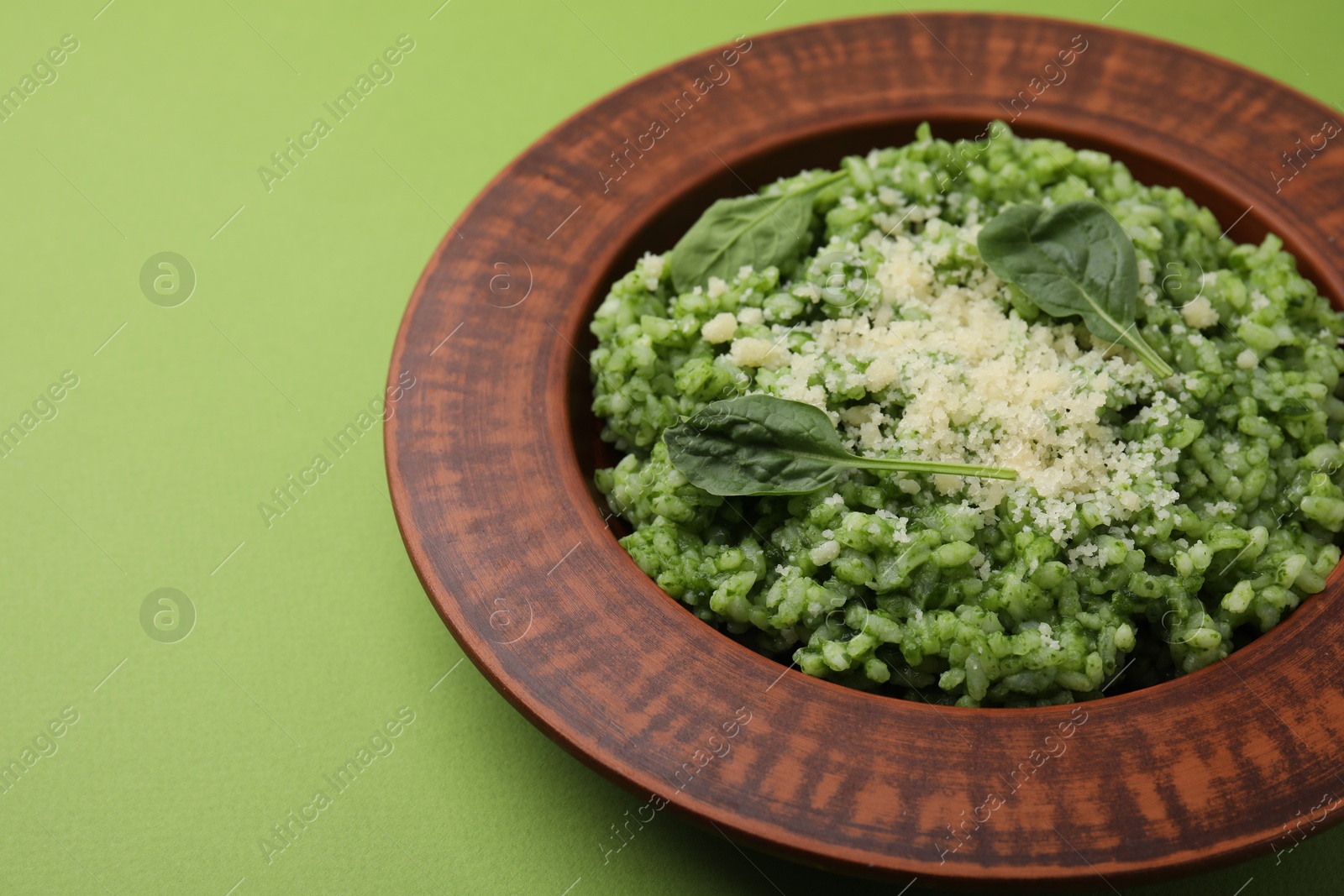 Photo of Delicious spinach risotto with parmesan cheese on light green background