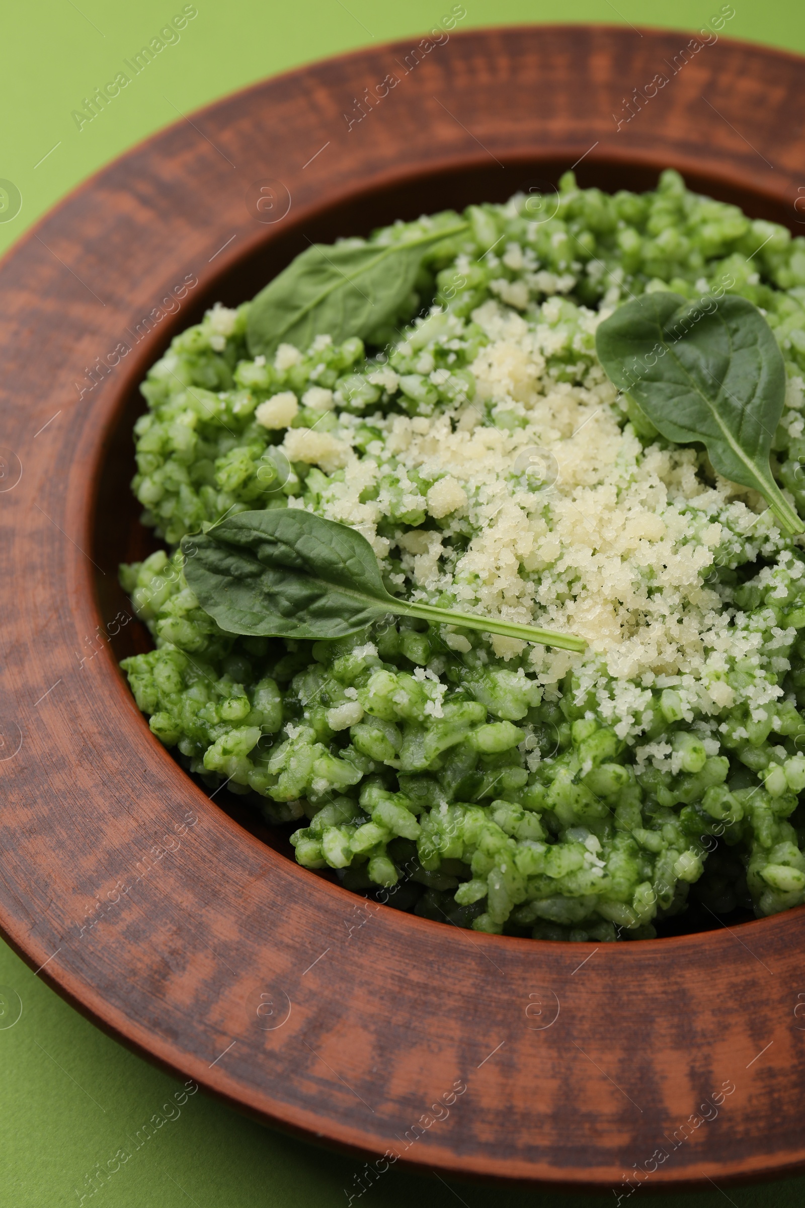 Photo of Delicious spinach risotto with parmesan cheese on light green background