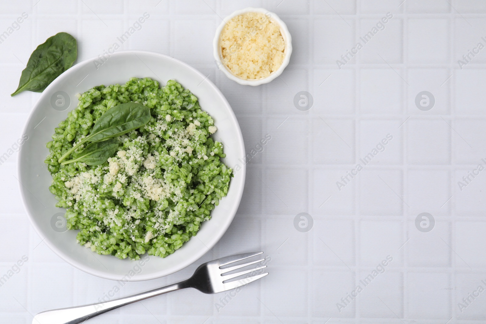 Photo of Delicious spinach risotto with parmesan cheese served on white tiled table, flat lay. Space for text