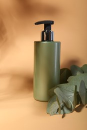 Photo of Shampoo in bottle and green eucalyptus leaves on pale orange background