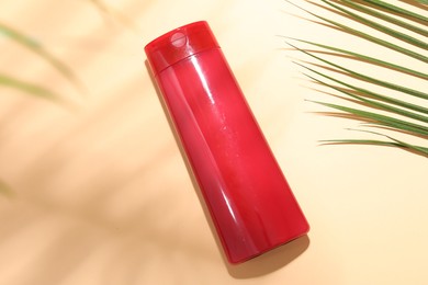 Photo of Shampoo in bottle and palm leaf on pale orange background, top view