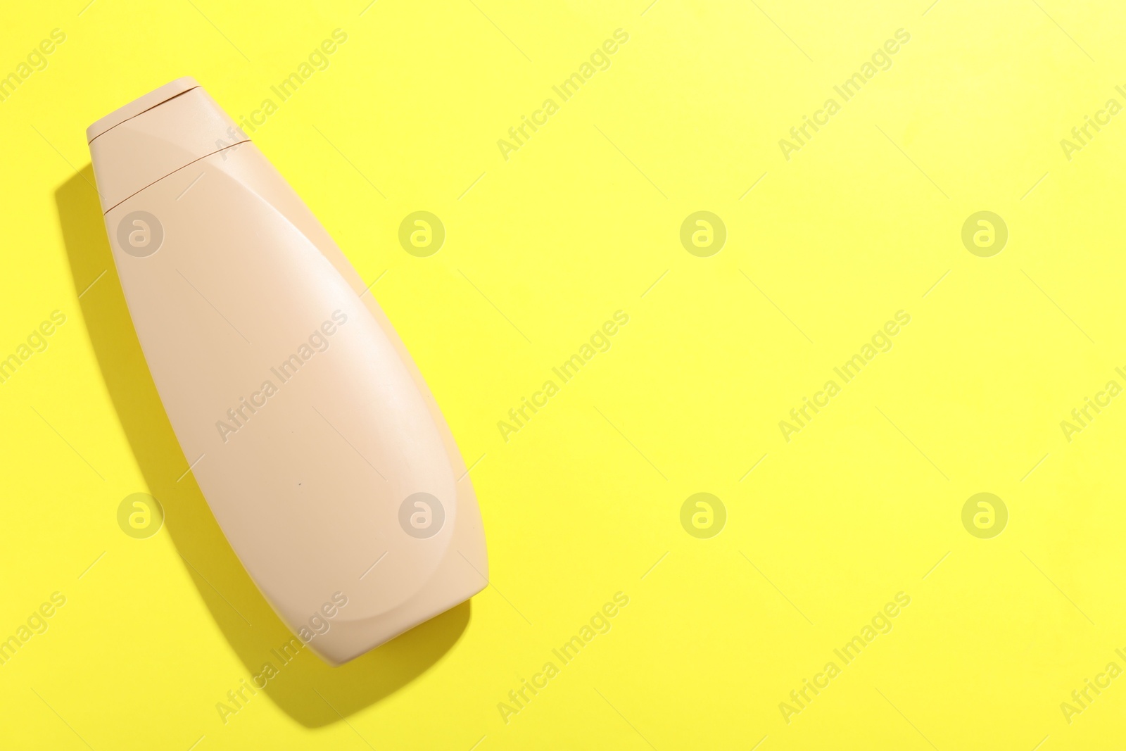 Photo of Shampoo in bottle on yellow background, top view. Space for text