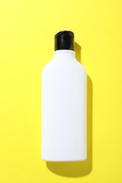 Shampoo in bottle on yellow background, top view