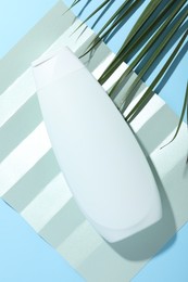 Shampoo in bottle and palm leaf on light blue background, top view