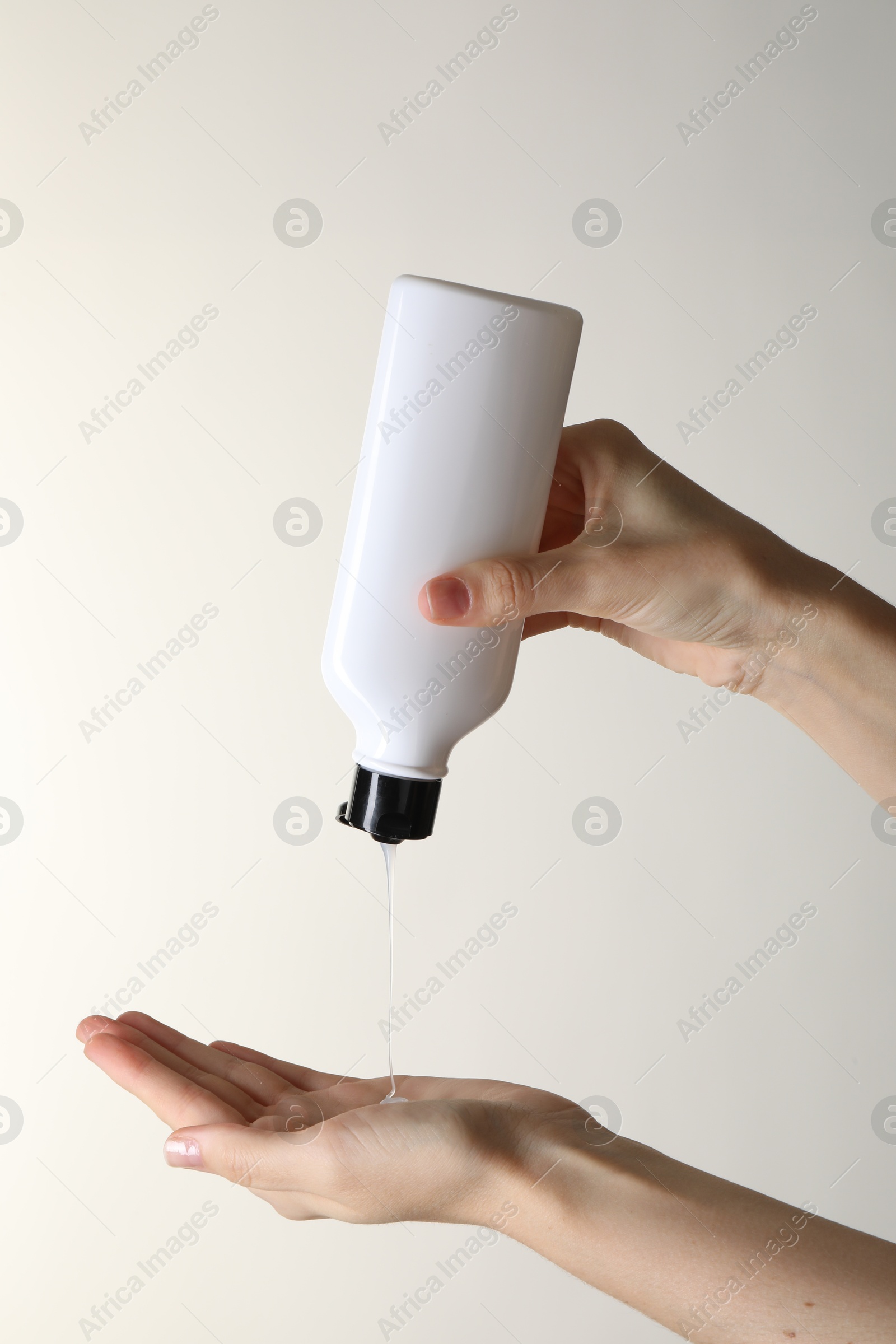 Photo of Woman pouring shampoo onto hand on beige background, closeup