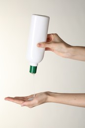 Photo of Woman pouring shampoo onto hand on beige background, closeup