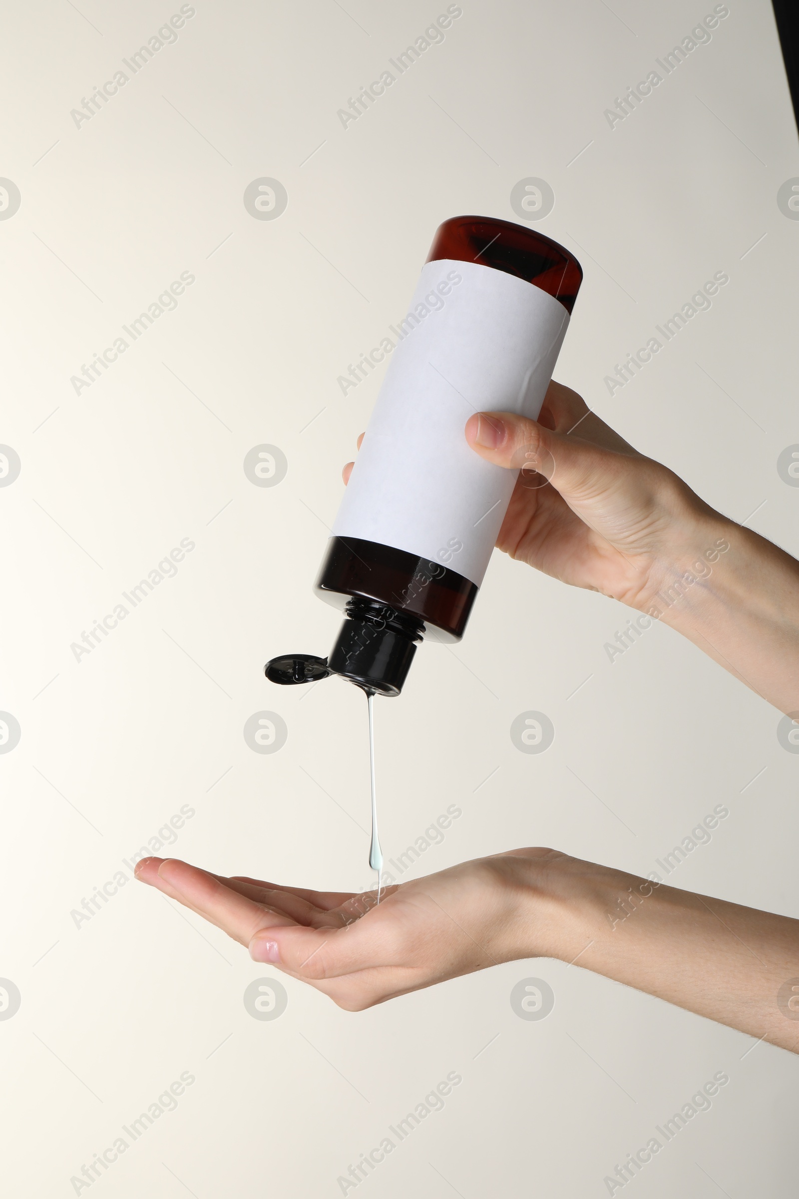 Photo of Woman pouring shampoo onto hand on beige background, closeup