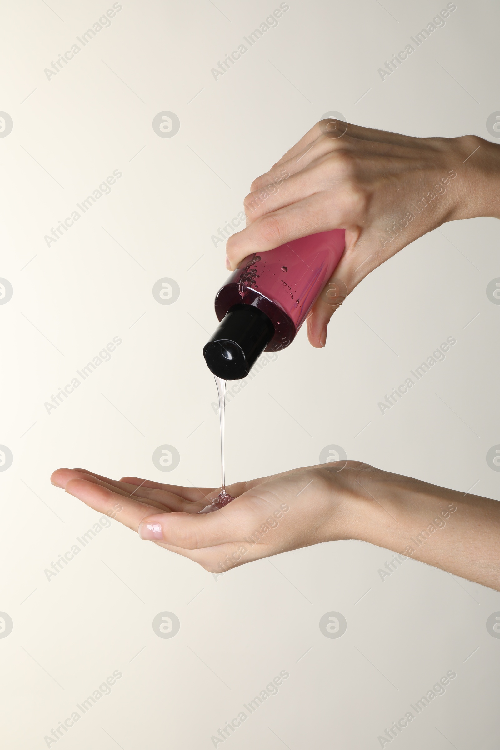 Photo of Woman pouring shampoo onto hand on beige background, closeup