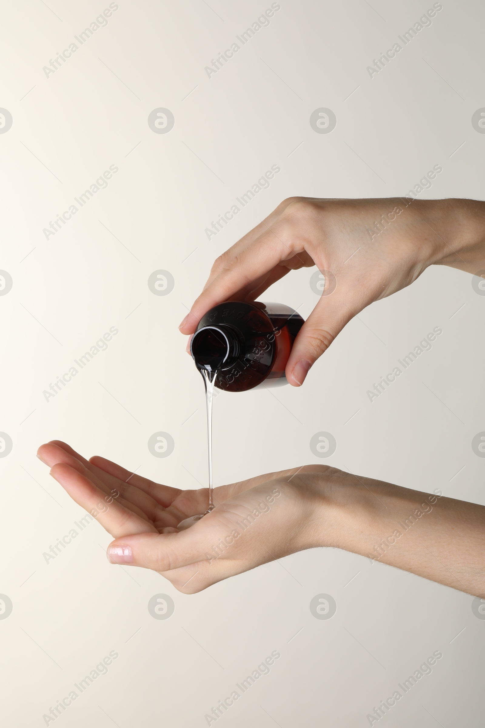 Photo of Woman pouring shampoo onto hand on beige background, closeup