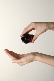 Woman pouring shampoo onto hand on beige background, closeup