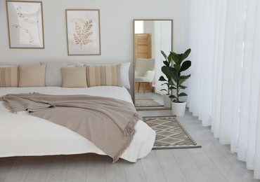 Photo of Large bed, houseplant and full-length mirror near window in room. Stylish bedroom interior