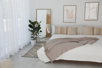 Photo of Large bed, houseplant and full-length mirror near window in room. Stylish bedroom interior