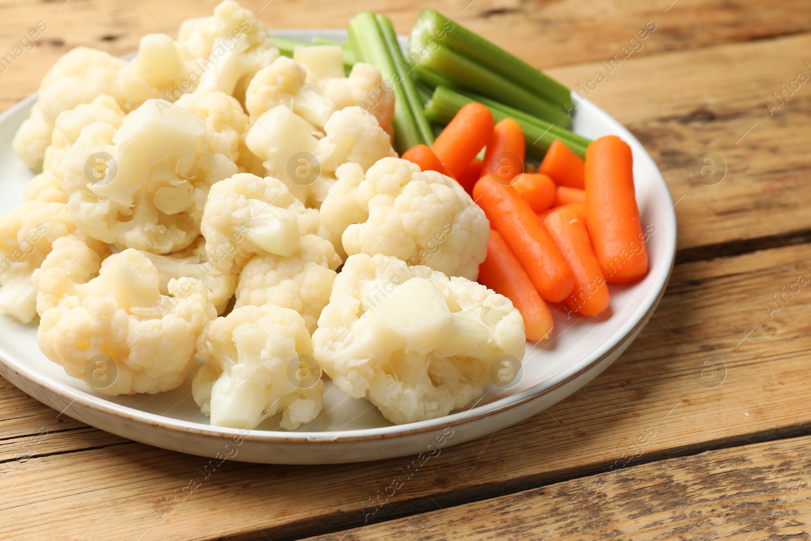 Photo of Tasty cauliflower with baby carrots and celery on wooden table, closeup