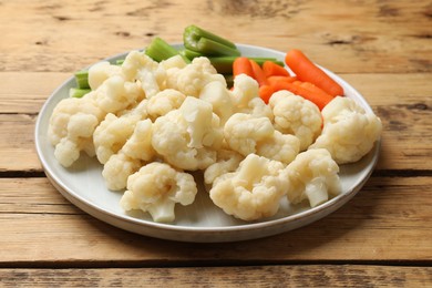 Photo of Tasty cauliflower with baby carrots and celery on wooden table, closeup