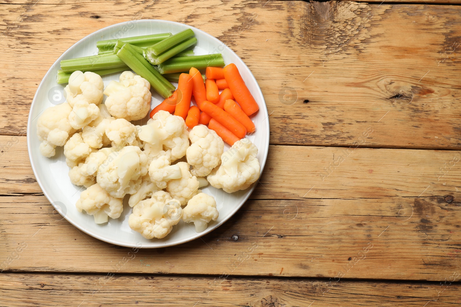 Photo of Tasty cauliflower with baby carrots and celery on wooden table, top view. Space for text