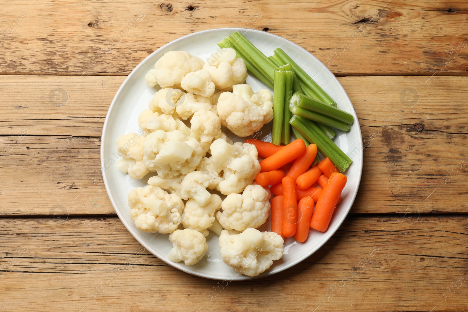 Photo of Tasty cauliflower with baby carrots and celery on wooden table, top view