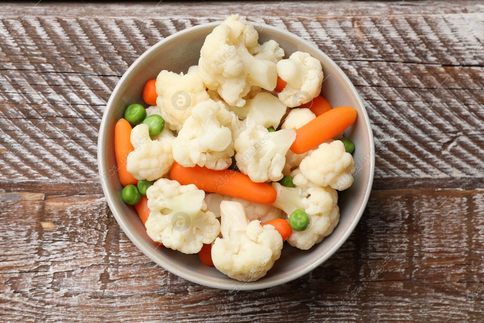 Photo of Tasty cauliflower with baby carrots and green peas on wooden table, top view