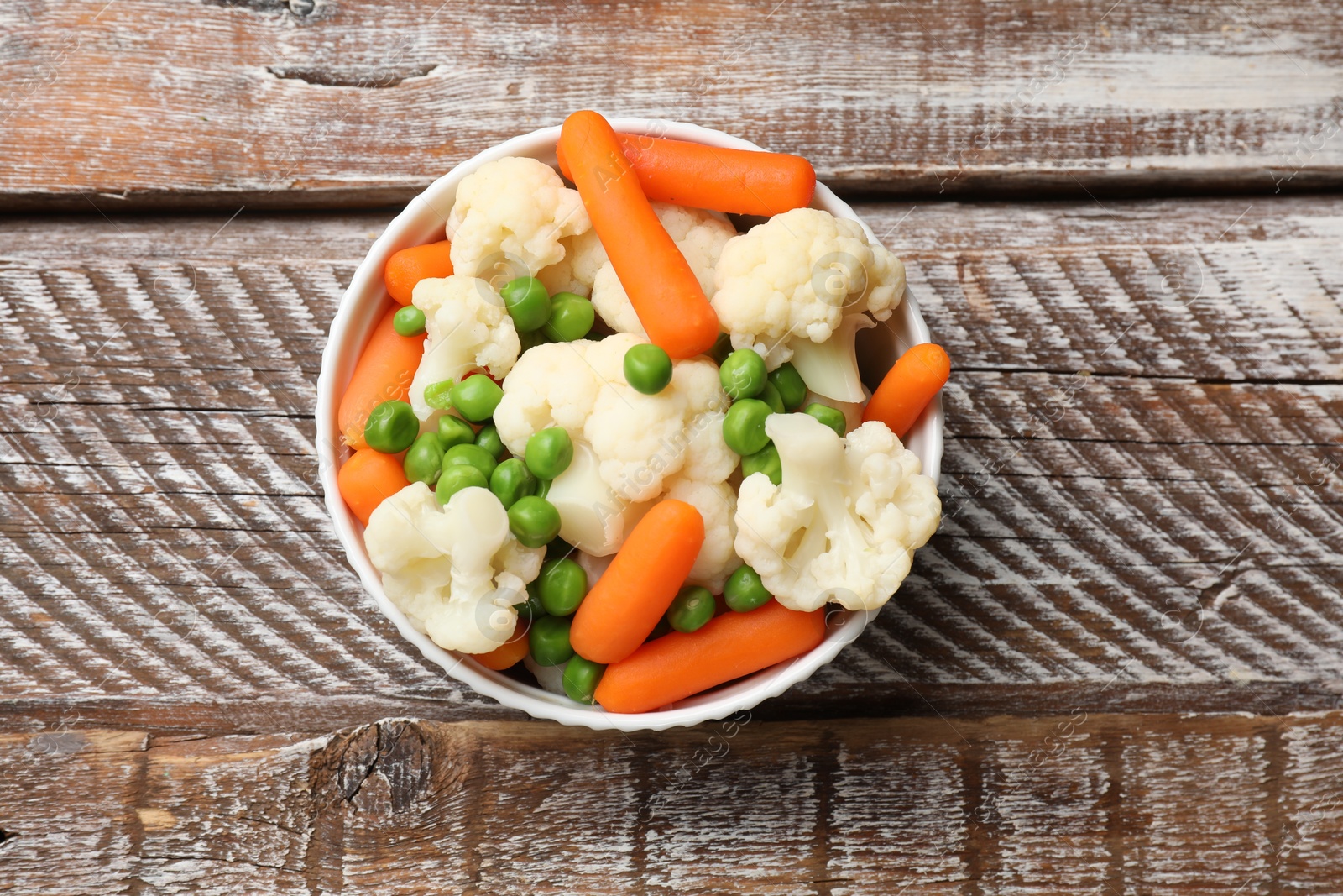 Photo of Tasty cauliflower with baby carrots and green peas on wooden table, top view