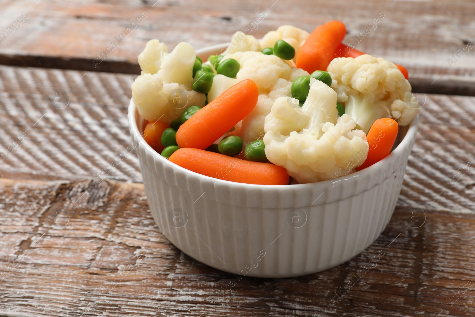 Photo of Tasty cauliflower with baby carrots and green peas on wooden table, closeup