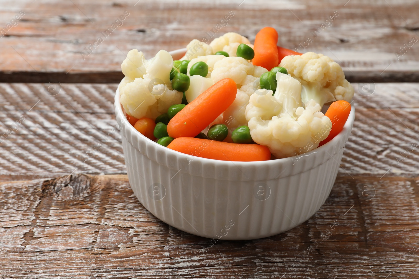 Photo of Tasty cauliflower with baby carrots and green peas on wooden table, closeup