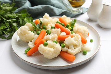 Photo of Tasty cauliflower with baby carrots and green peas on white table, closeup