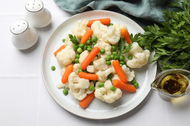 Photo of Tasty cauliflower with baby carrots and green peas on white tiled table, flat lay