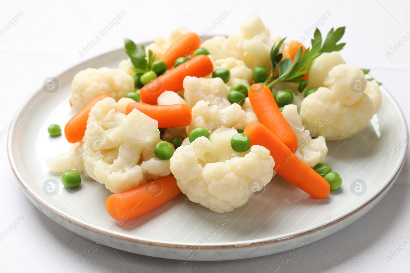 Photo of Tasty cauliflower with baby carrots and green peas on white table, closeup