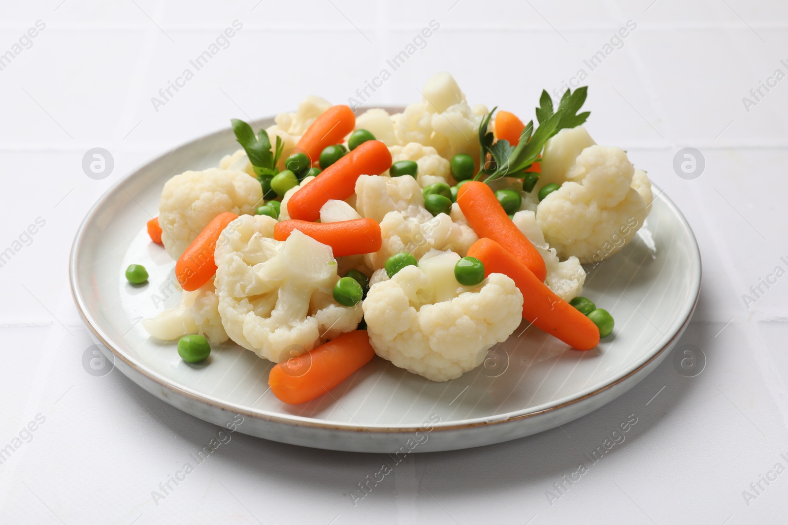 Photo of Tasty cauliflower with baby carrots and green peas on white table, closeup