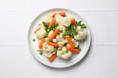 Photo of Tasty cauliflower with baby carrots and green peas on white tiled table, top view