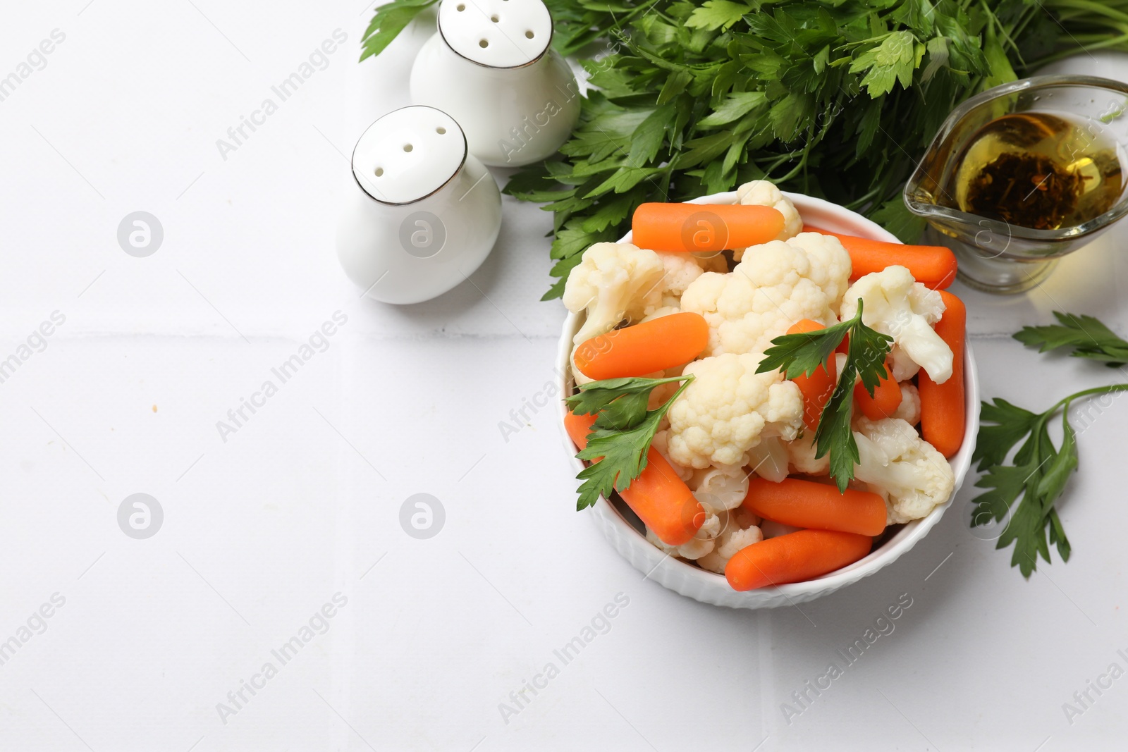 Photo of Tasty cauliflower with baby carrots and parsley on white tiled table, flat lay. Space for text