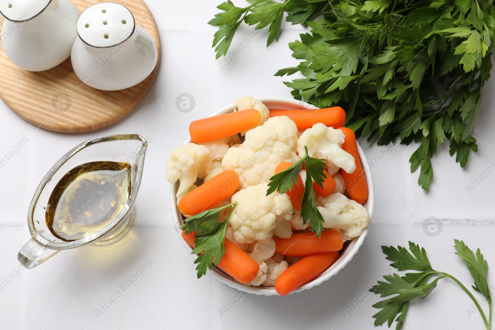 Photo of Tasty cauliflower with baby carrots and parsley on white tiled table, flat lay