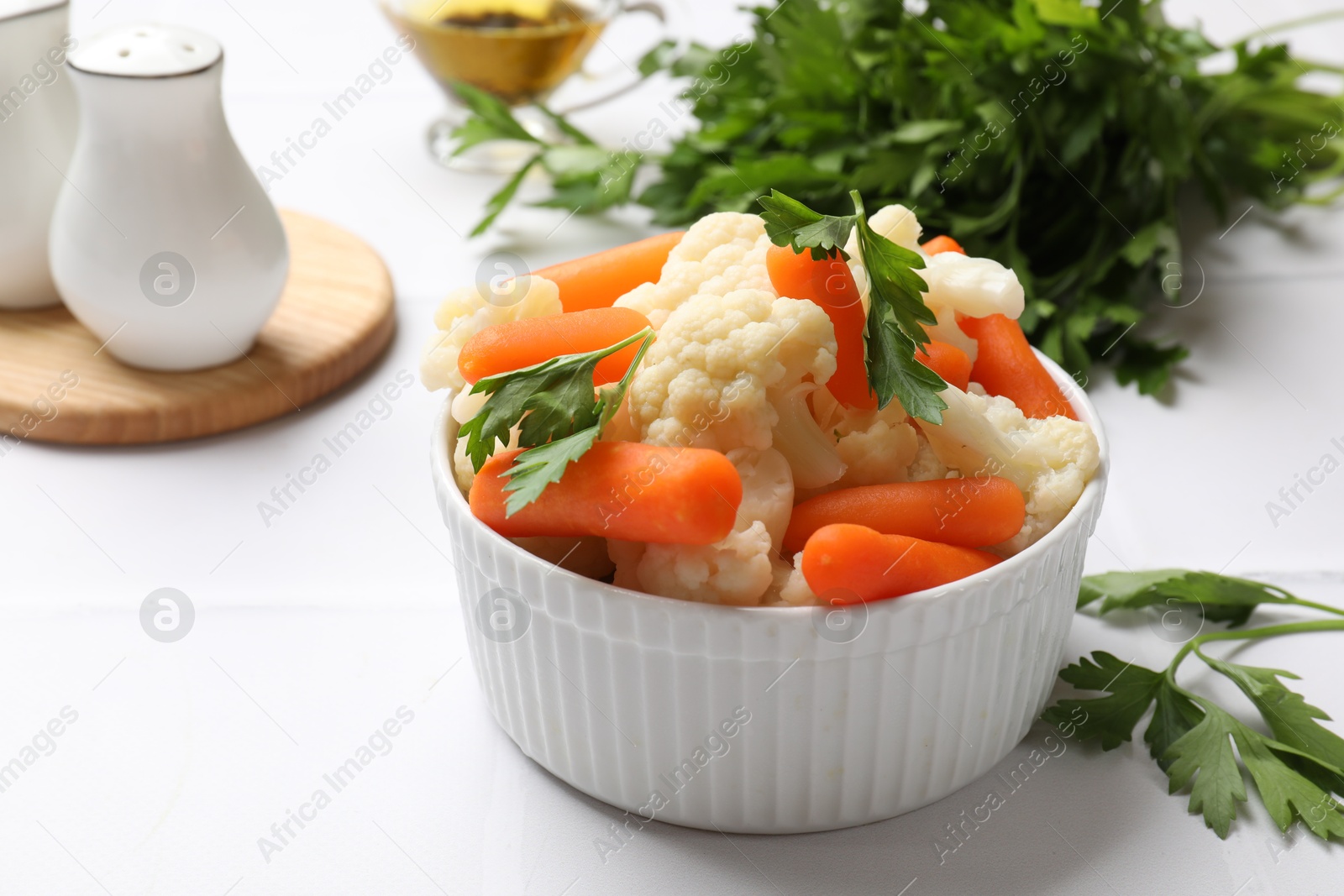 Photo of Tasty cauliflower with baby carrots and parsley on white table, closeup