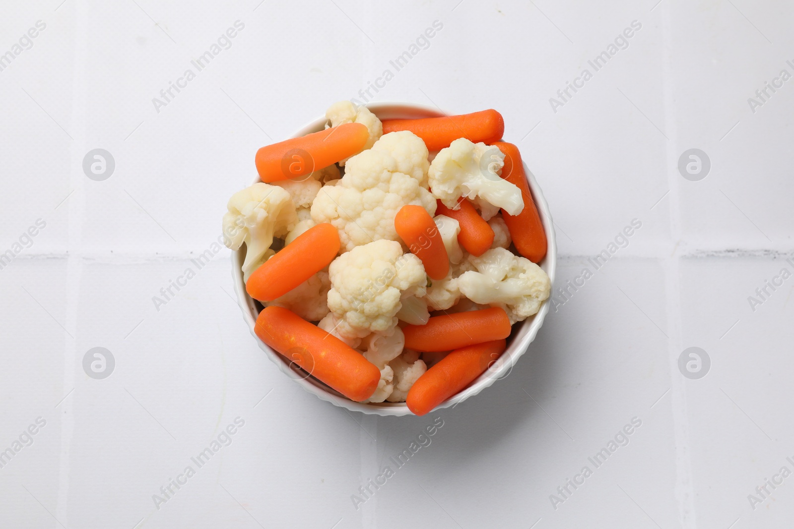 Photo of Tasty cauliflower with baby carrots on white tiled table, top view