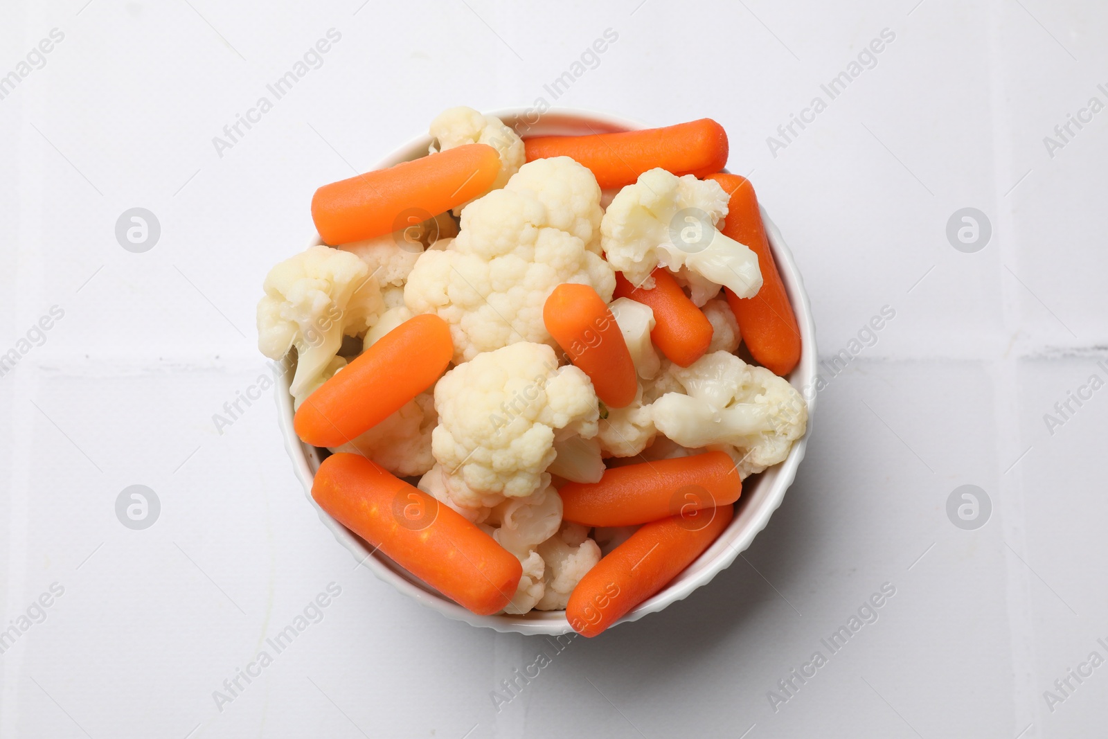 Photo of Tasty cauliflower with baby carrots on white tiled table, top view