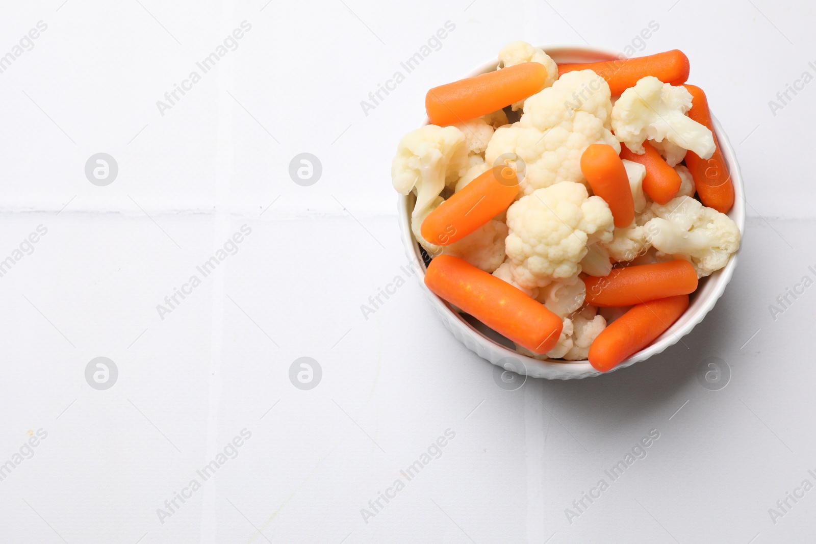 Photo of Tasty cauliflower with baby carrots on white tiled table, top view