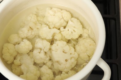 Photo of Cooking cauliflower. Florets in white pot with water on cooktop, closeup